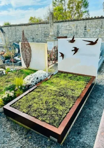 Sépulture moderne avec cadre en acier corten, stèle blanche ornée d'oiseaux et jardinière végétale